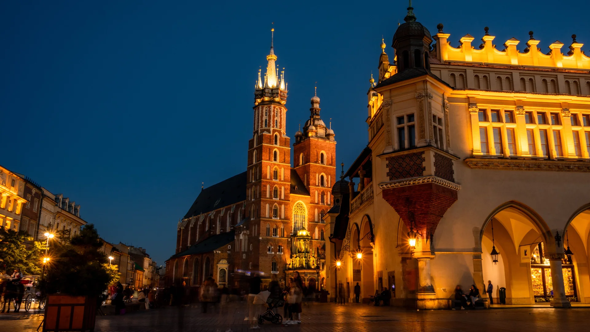 St Mary's Basilica and the Cloth Hall in Kraków's Main Market Square at blue hour, lit gold against a deep blue sky